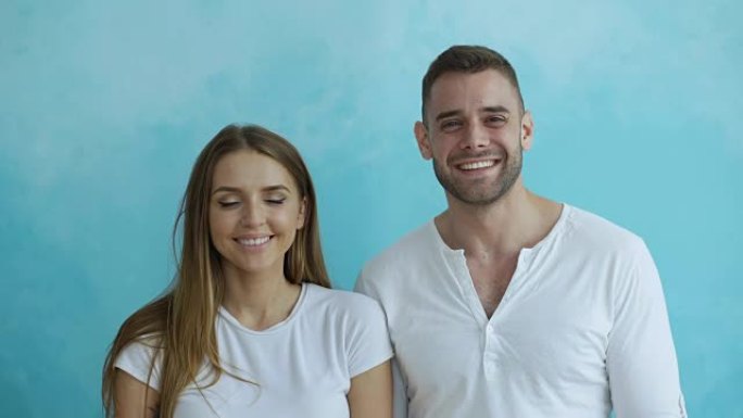 蓝色背景下年轻幸福的夫妇微笑着笑着对着镜头的肖像