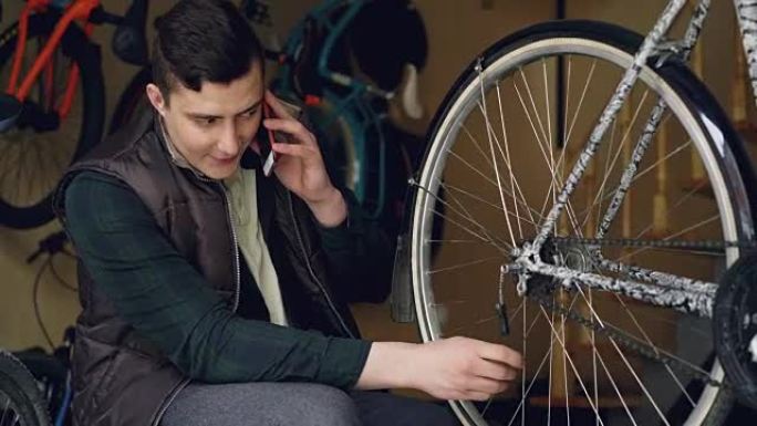 开朗的维修人员在自行车rapair车间工作时正在手机上聊天，检查车轮辐条和转动车轮。修复和沟通理念。