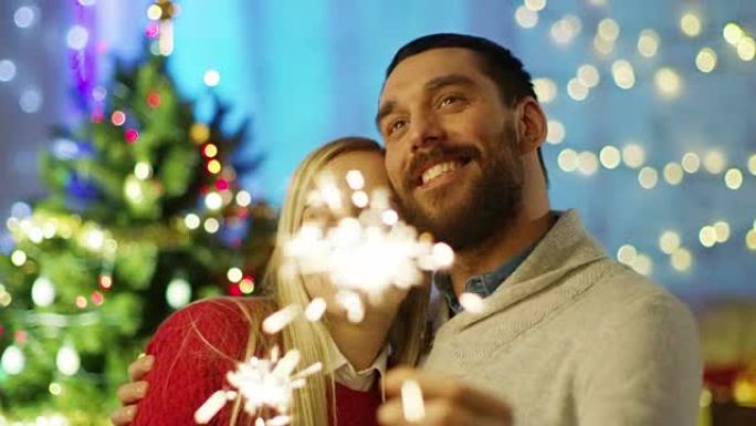 幸福的夫妇点燃火花和微笑。背景圣诞树和装饰有灯的房间。