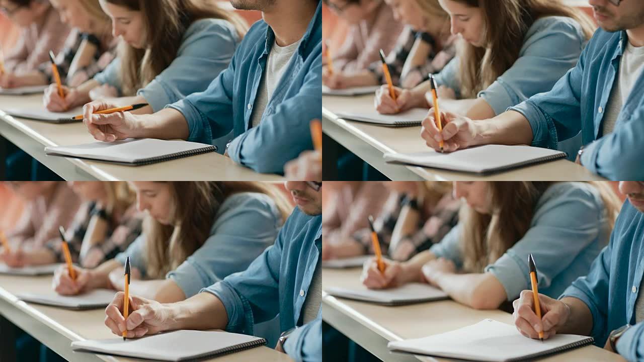 教室里一排多民族学生参加考试/测试的移动镜头。专注于拿笔和在笔记本上书写。聪明的年轻人在大学学习。