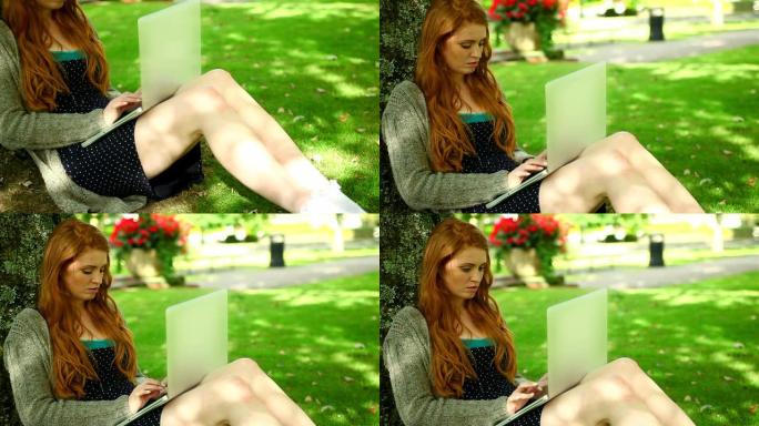 可爱的红发女郎用她的笔记本坐在草坪上