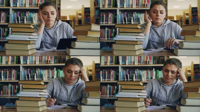美丽的白人少女正坐在大学图书馆的桌子旁，拿着数字平板电脑。她又累，摇头写字帖