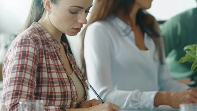 女人在激烈的讨论中坐在会议桌旁做笔记。