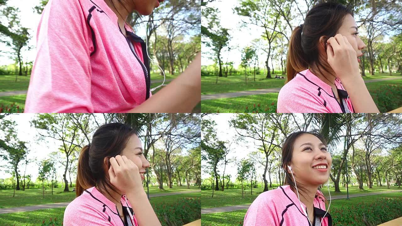 慢动作-快乐的年轻亚洲女性在公园晨练前通过伸展身体来热身。年轻的亚洲女性通过听音乐来放松自己。户外运