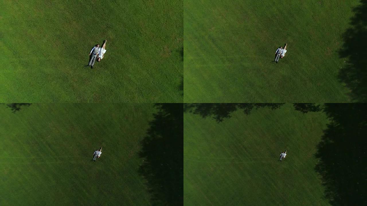 空中自上而下: 激动的怀孕夫妇躺在草地上牵着手