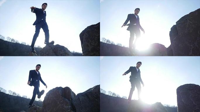 穿着西装的亚洲男子在海边的岩石上行走和平衡。跨过大石头。