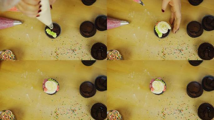 年轻女子用彩色奶油装饰巧克力纸杯蛋糕的俯视图。女性使用糕点袋