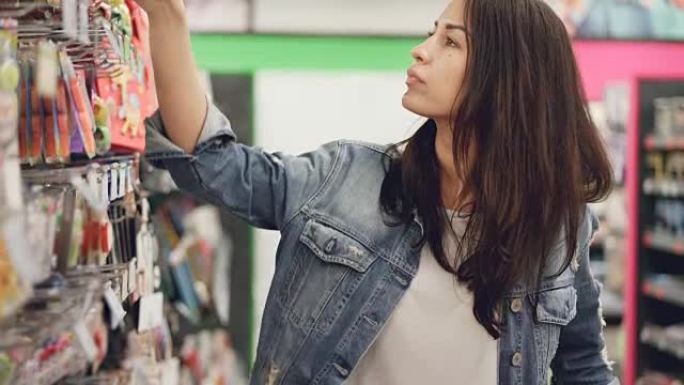 迷人的年轻女子正在超市购买生日蜡烛，她正在取货，看着它们并进行比较。购物和人的概念。
