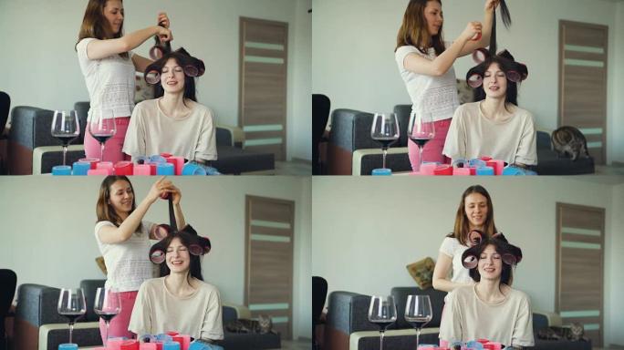 两个快乐的女人朋友互相取笑卷发器发型，在家玩得开心