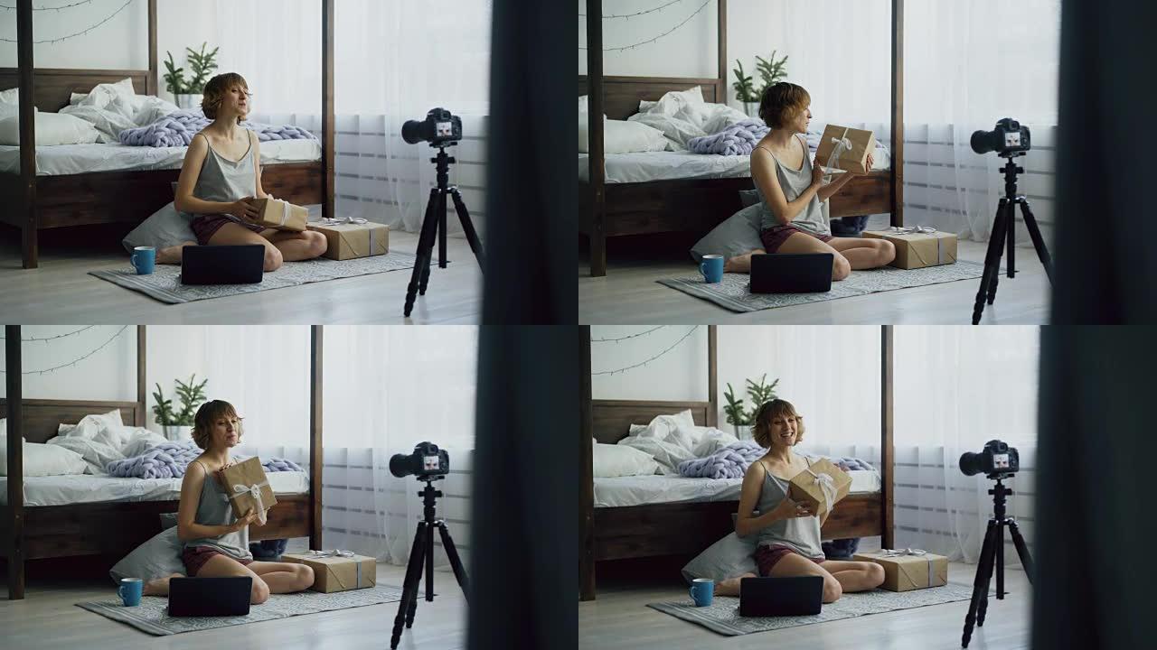 迷人的年轻女子坐在床边录制视频博客关于用dslr相机包装礼品盒