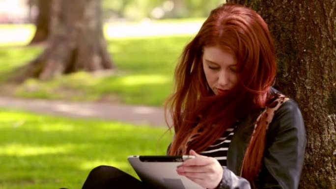在公园里使用平板电脑的漂亮红发女郎