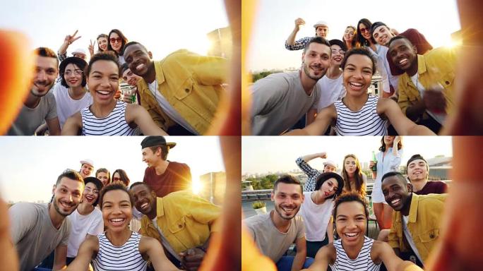 非裔美国女孩拿着相机，在屋顶派对上与快乐的朋友自拍的视点镜头。男人和女人看着相机，摆姿势大笑。