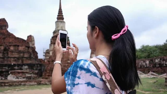 在泰国大城府历史公园使用智能手机拍照和社交媒体的亚洲女性旅行者
