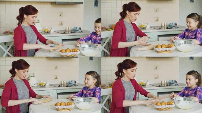 年轻的母亲在周末在厨房做饭时滚动面团并与可爱的小女儿交谈。家庭、食物、家庭和人的概念