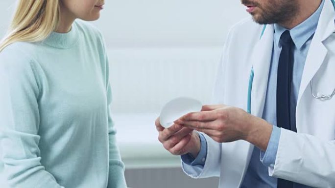 整形/美容外科医生向女性患者展示了她未来手术的乳房植入物样本。从事个人计算机分析吸脂手术数据的护士。