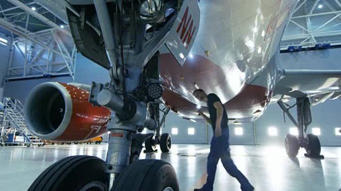 在机库中，飞机维修工程师/技术员/机械师目视检查飞机的底盘和在其下方行走的机身/机身。