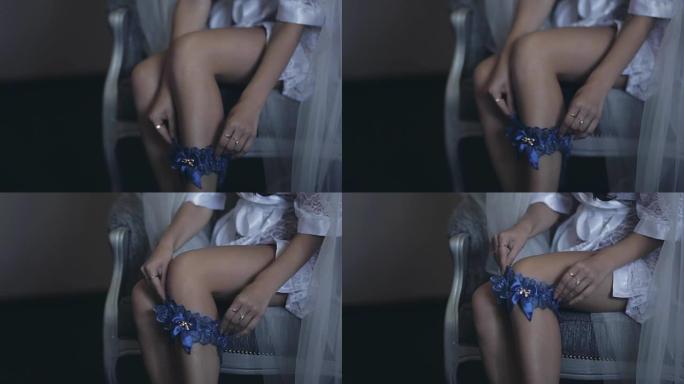 穿着白色内衣的性感新娘的特写镜头，peignoir坐在椅子上，穿上蓝色吊袜带。婚礼前的早晨