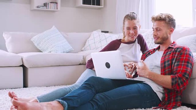 年轻的白人夫妇坐在家里的地板上使用笔记本电脑