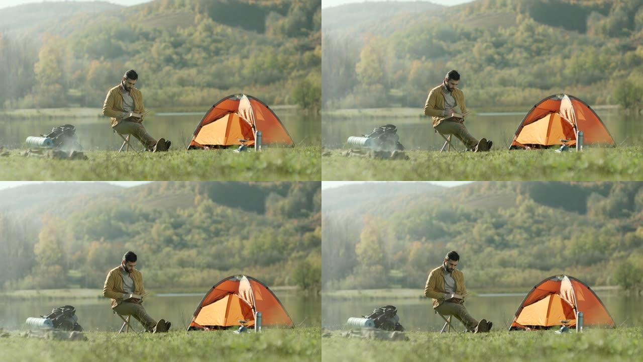 男人坐在湖边的帐篷旁看书