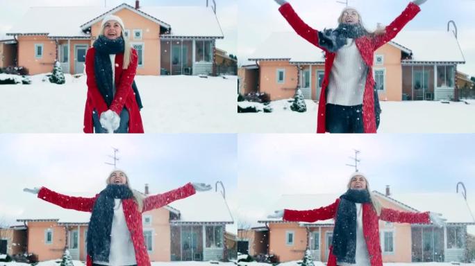 快乐的年轻微笑的女人把雪抛向空中。穿红外套戴围巾的女孩在自家后院享受冬天。