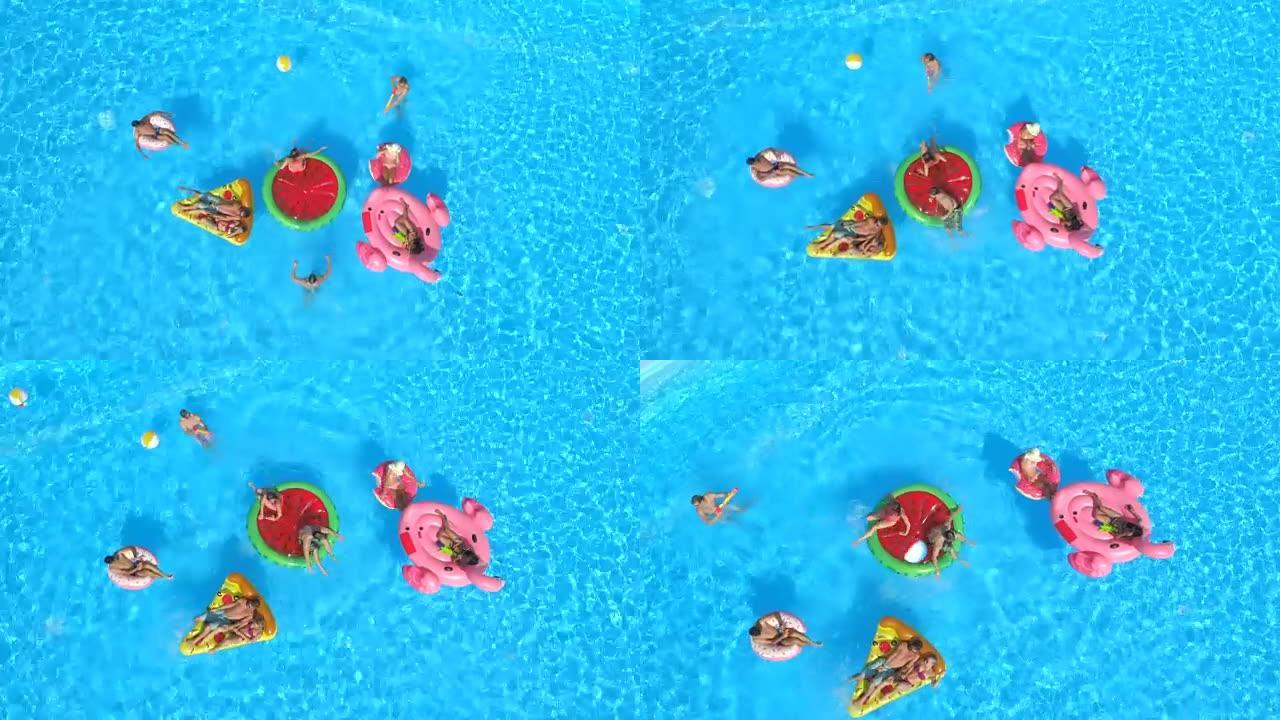空中: 顽皮的青少年在泳池水中充气的彩色浮标上玩乐