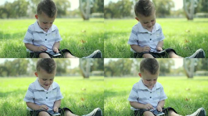 在公园使用手机触摸屏的年轻可爱的男婴。