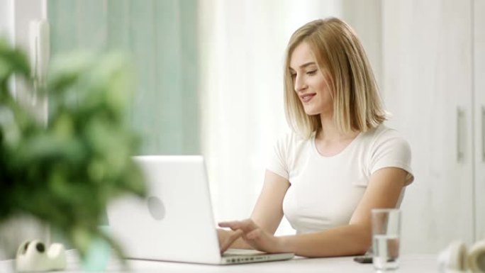 微笑的女孩在笔记本电脑上打字，提高了视野，并在相机前竖起大拇指