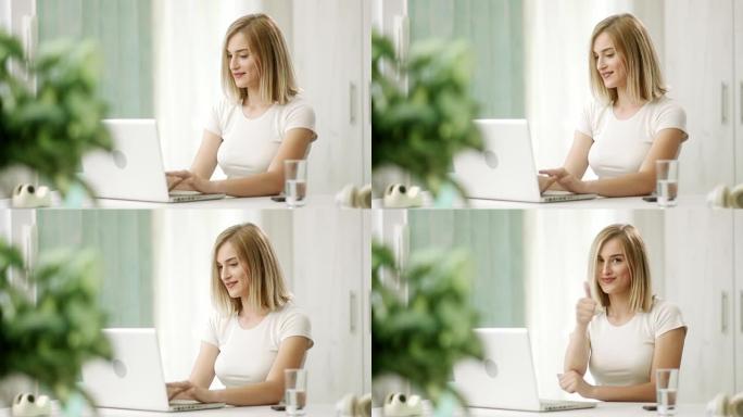 微笑的女孩在笔记本电脑上打字，提高了视野，并在相机前竖起大拇指