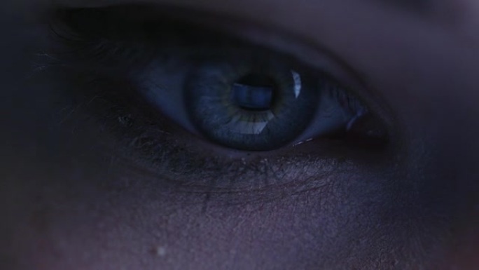 女人的眼睛在黑暗中凝视着工作的平板电脑屏幕的特写镜头。