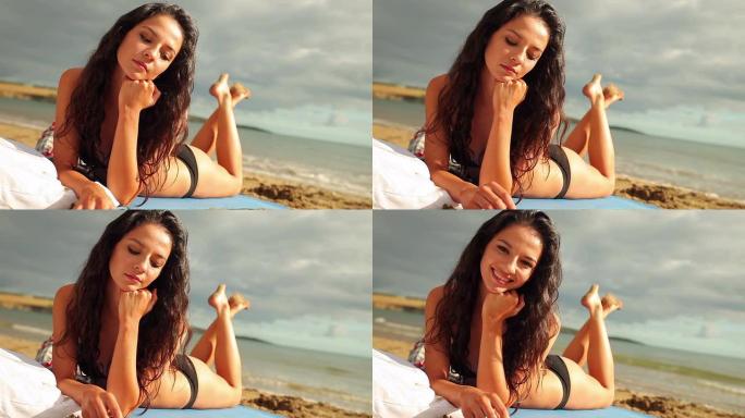 快乐的黑发女人躺在沙滩上对着镜头微笑