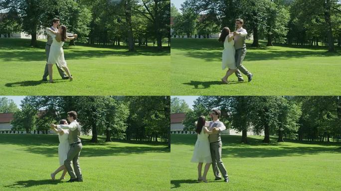 慢动作: 年轻夫妇在温暖的晴天在绿色公园快乐地跳华尔兹