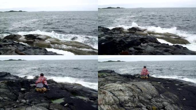 男子背包客旅行者在多岩石的海岸上休息。无人机的观点