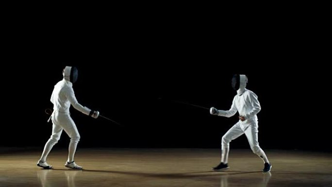 两名专业击剑手熟练地用箔纸战斗。拍摄孤立在黑色背景上。