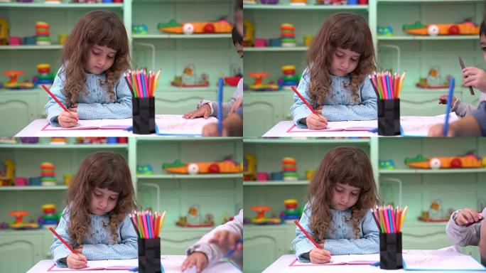 学龄前女孩在桌子上的朋友在书上画画
