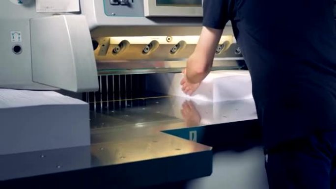 一名员工正在将两大堆纸放在切刀下，将它们分为四个部分。