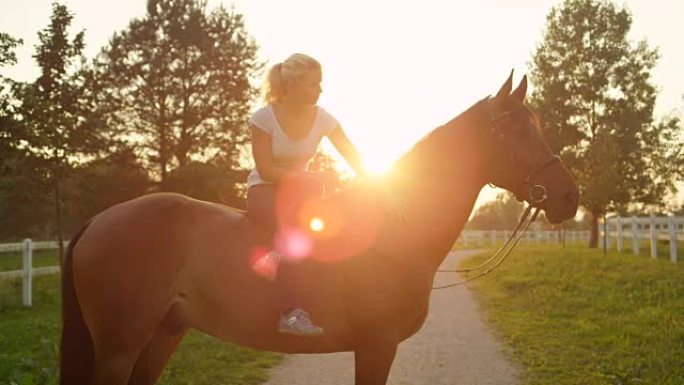 在阳光明媚的夜晚，慢动作的年轻女子坐在一匹马上，双腿交叉