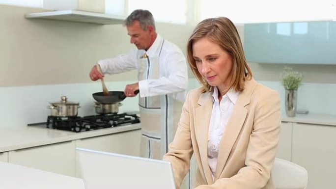 女商人在丈夫做饭时使用笔记本电脑