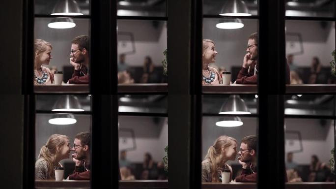 透过窗户看。年轻夫妇坐在咖啡馆里，喝咖啡，聊天，晚上一起玩乐