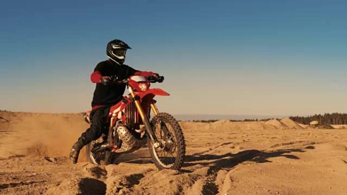 专业的FMX摩托车骑手旋转全油门手柄，开始在沙地越野赛道上骑行。风景优美的日落。
