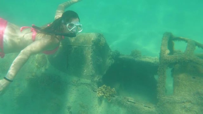 水下: 年轻女子探索飞机的残余物并看着相机。