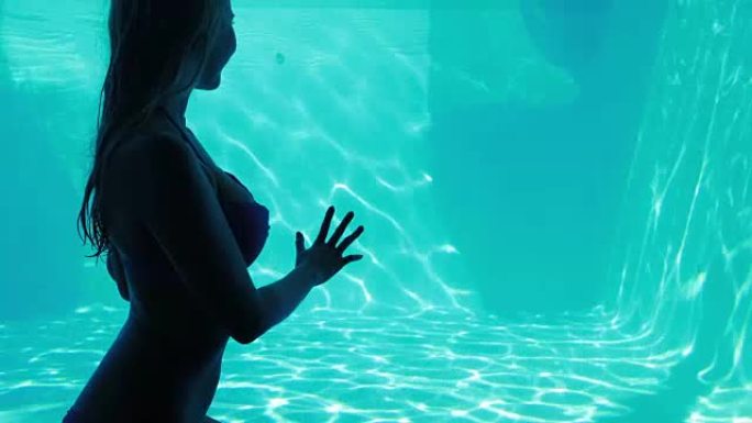 迷人的女人透过玻璃看着游泳池