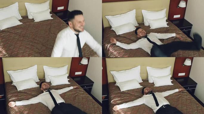快乐商人的俯视图慢动作在酒店房间的床上跳跃，躺着轻松的微笑。商务、旅行和人的概念