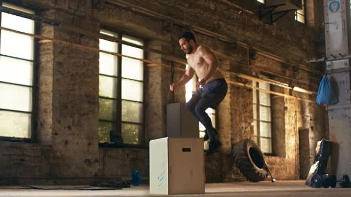 肌肉赤裸的健美男子在硬核健身房做他的健身训练计划的一部分。男人因剧烈运动而汗流浃背，健身房位于风景如