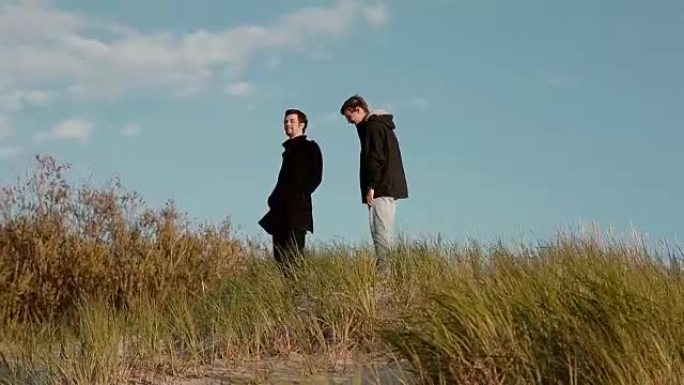 两个年轻人正从沙丘上聊天和微笑着走下来