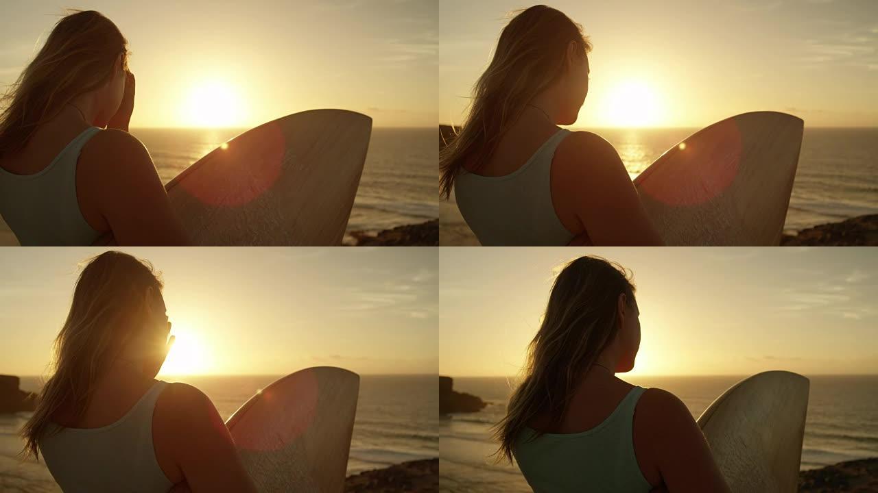 慢动作镜头耀斑: 拿着冲浪板的女人在风中调整头发。