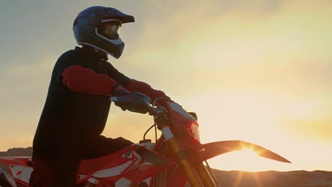 专业FMX摩托车骑手准备开始驾驶他的摩托车在坚硬的沙地越野地形。太阳设置。