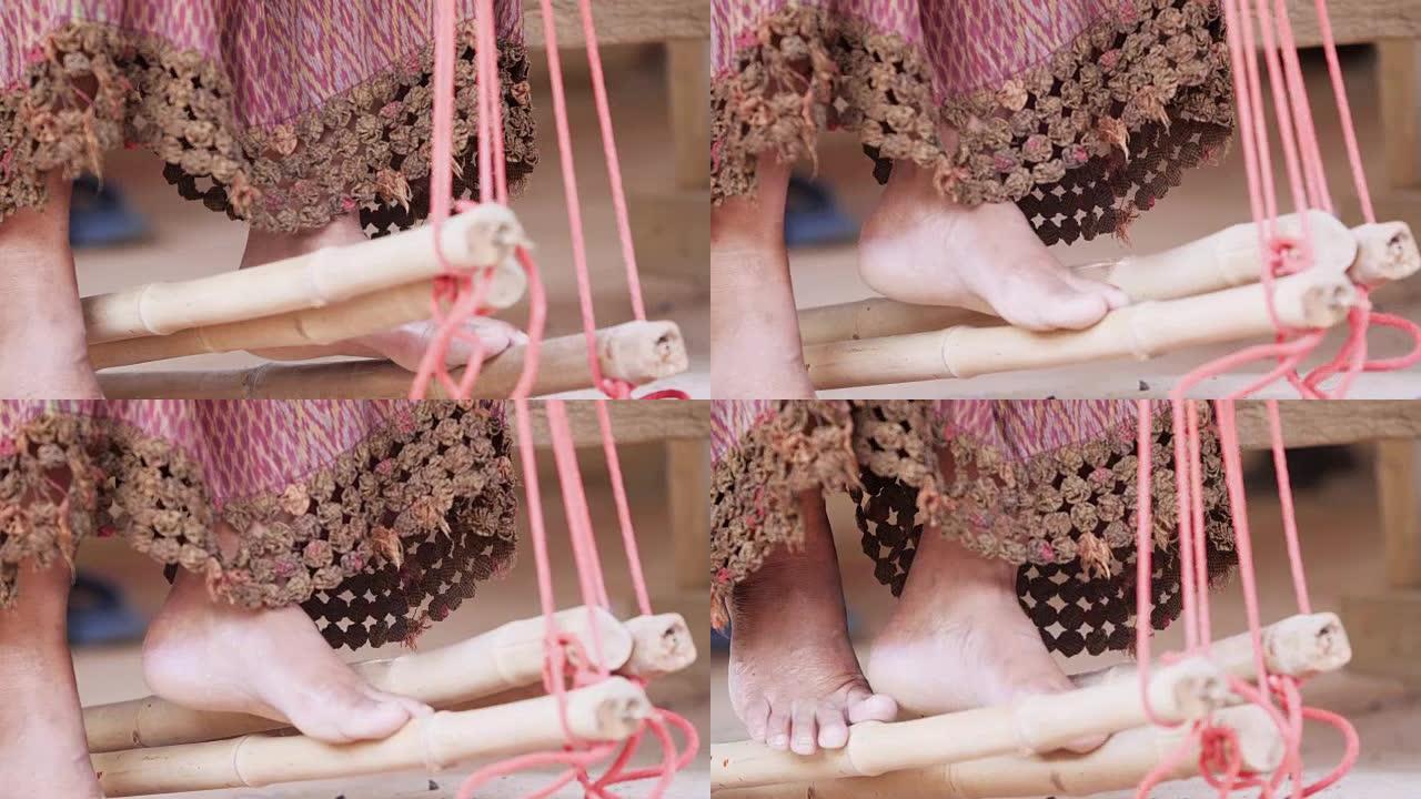 传统的泰国纺织品制造商在工艺村，老妇女在木制编织线机上工作，并纺纱制作棉织物。
