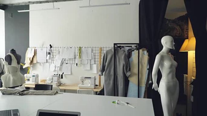 轻盈服装设计工作室的全景照片，配有大型裁缝办公桌、人体模型、钉在墙上的众多草图、缝纫机和铁轨上的半成