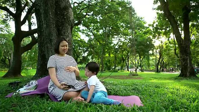 有孩子在户外的孕妇。夏天公园里自然背景的母子俩。抱着母亲的小男孩，第二次怀孕。怀孕，新生活，家庭，父