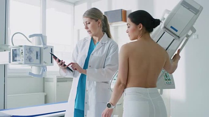 在医院，女性患者听乳房x线摄影技术专家/医生使用平板电脑，解释乳腺癌预防的重要性。乳房x光检查程序。